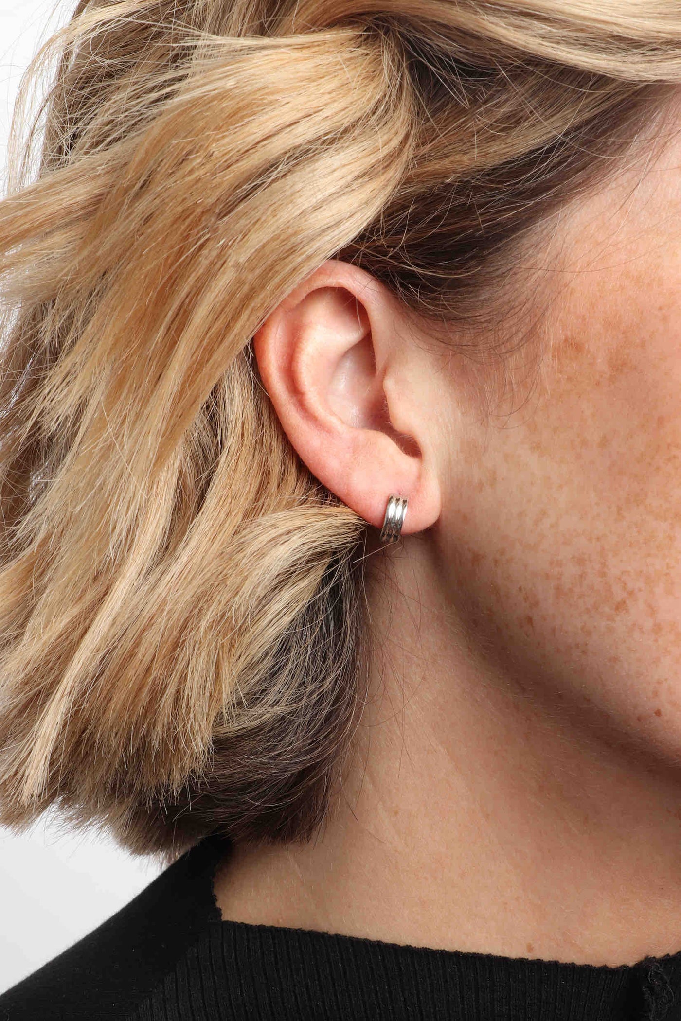 Marrin Costello wearing Marrin Costello Jewelry Evelyn 3mm Huggies ribbed small hoops with click tension hinge closure— for pierced ears. Waterproof, sustainable, hypoallergenic. Polished stainless steel.