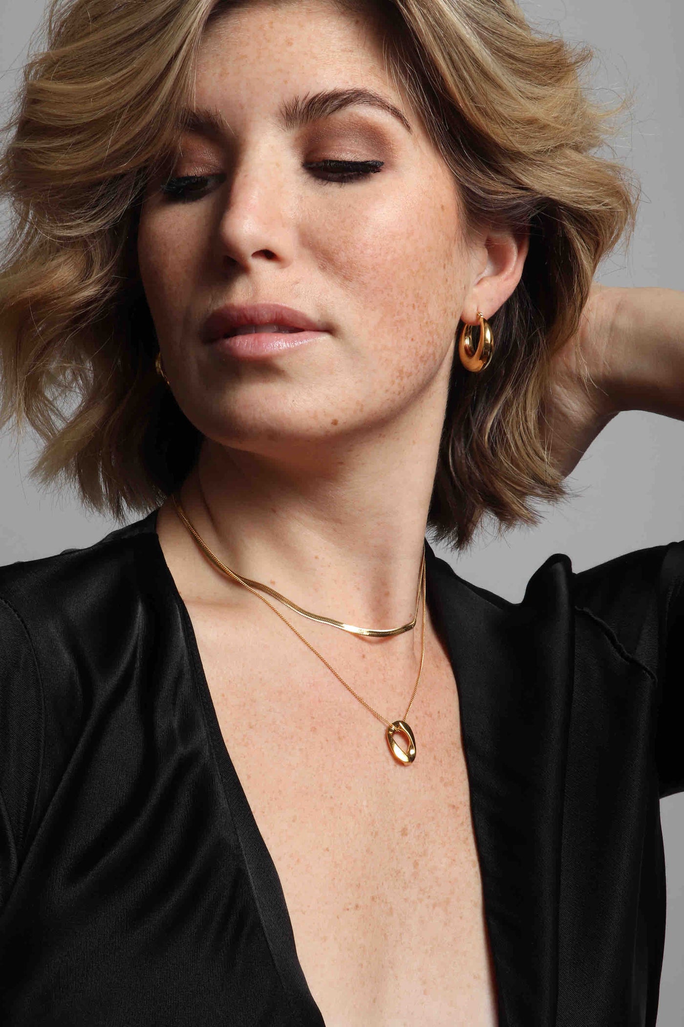 Delicate 14k gold plated stainless steel jewelry by Marrin Costello, featuring our click hoop round Layla Hoops, vintage inspired herringbone Ramsey Choker in 3mm width, and Cuban Link Queens Pendant on a delicate curb link chain, styled with a vintage black silk wrap dress 
