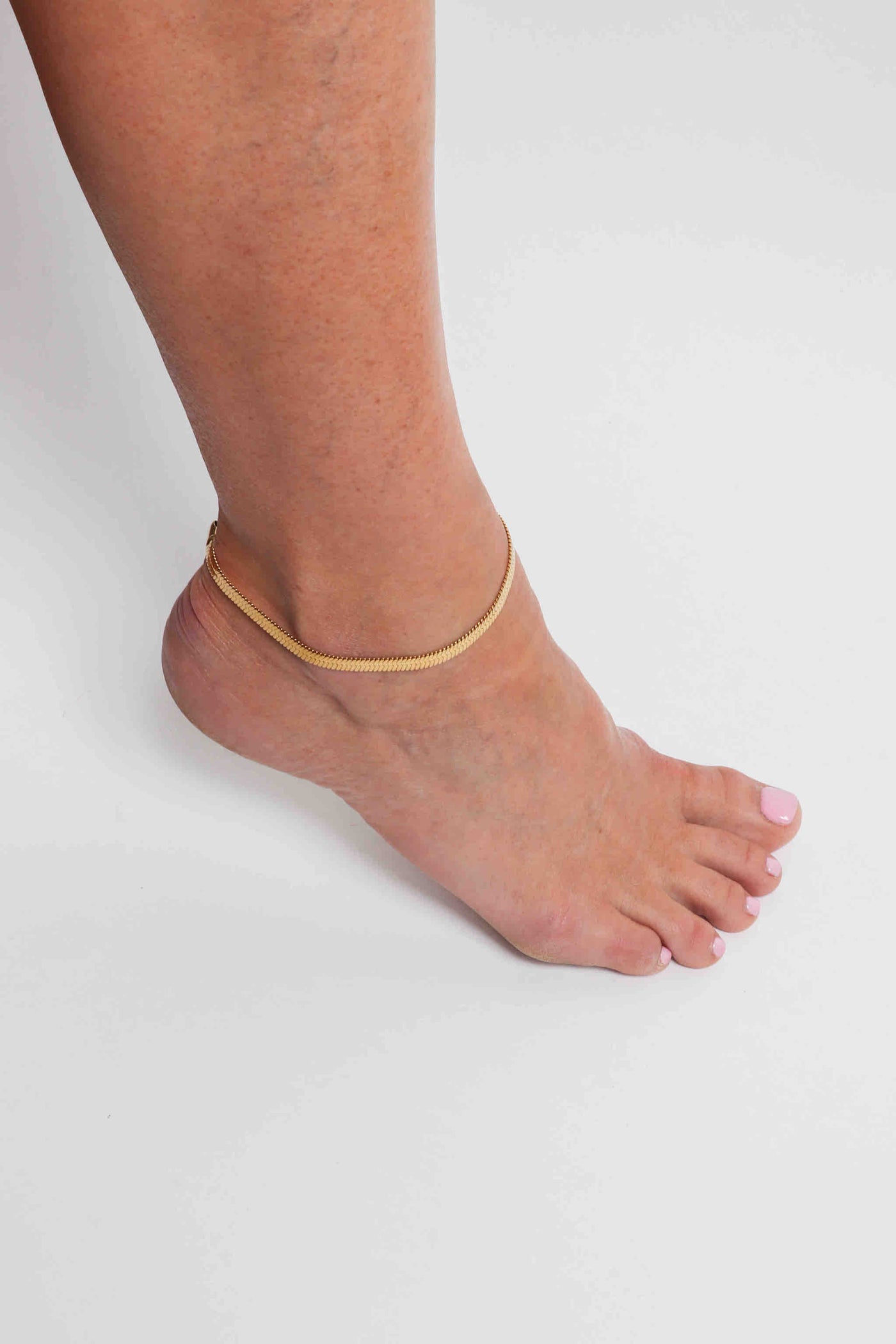 Marrin Costello wearing Marrin Costello Jewelry 5mm thick herringbone snake chain anklet with lobster clasp closure. Waterproof, sustainable, hypoallergenic. 14k gold plated stainless steel.