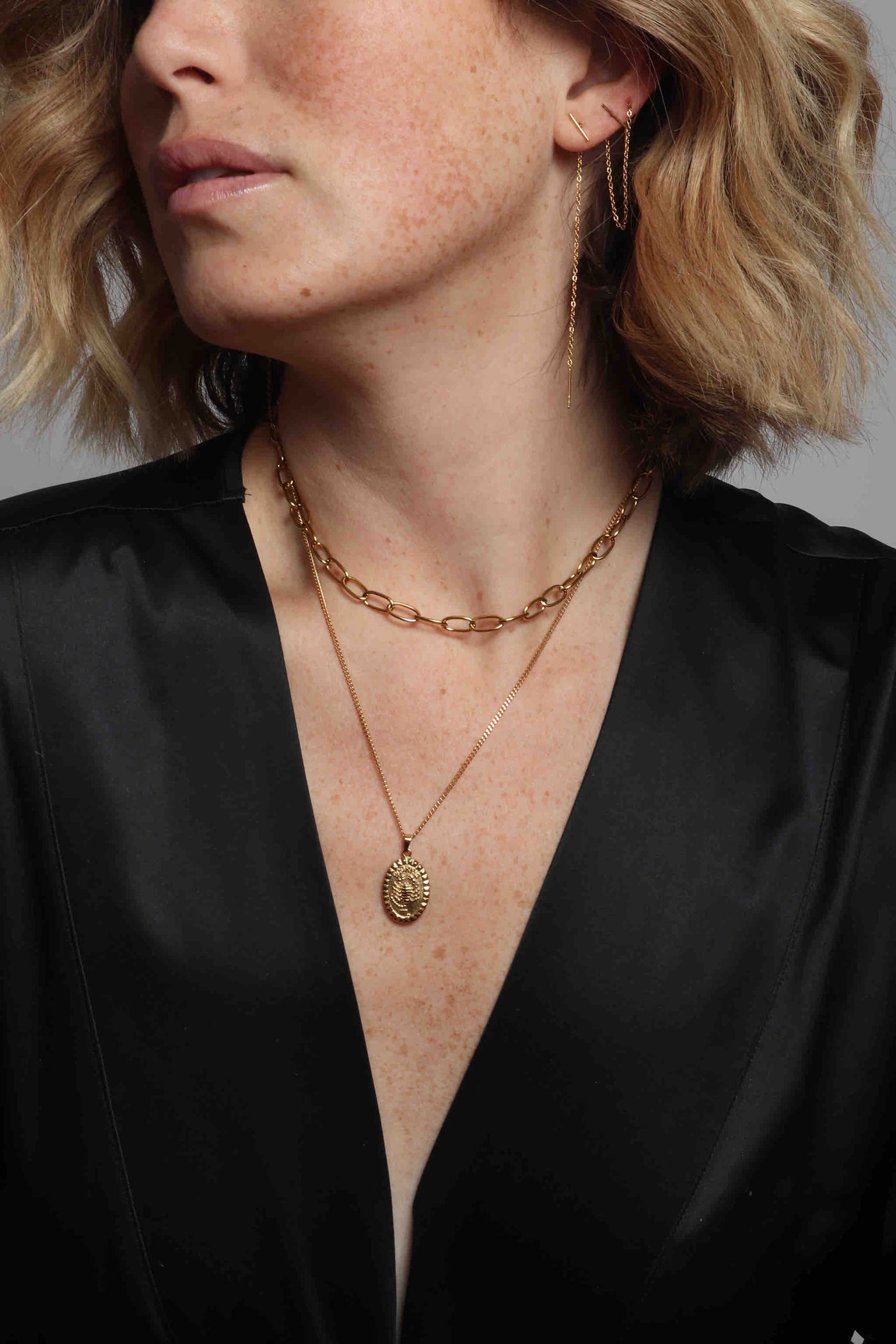 Delicate 14k gold plated stainless steel jewelry by Marrin Costello, featuring our bar and chain Nile threader earrings, oval link adjustable Anita Choker, and hand carved oval zodiac pendant with our signature Melrose stud detail, styled with a silk robe by Third Love and a vintage belt from Recess LA